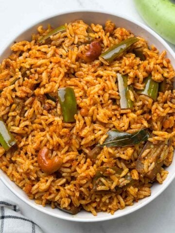 vangi bhath rice served in a bowl with green brinjals on the side