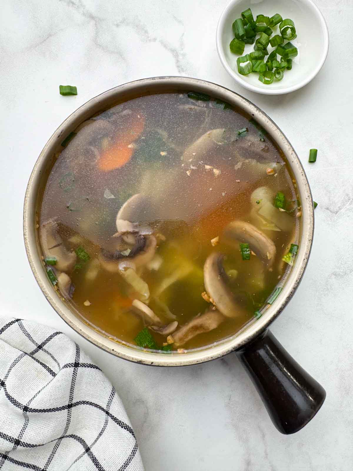 healthy vegetable clear soup served in a soup bowl with spring onions on the side