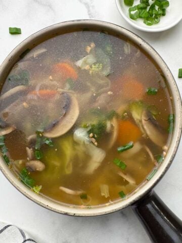 healthy vegetable clear soup served in a soup bowl with spring onions on the side