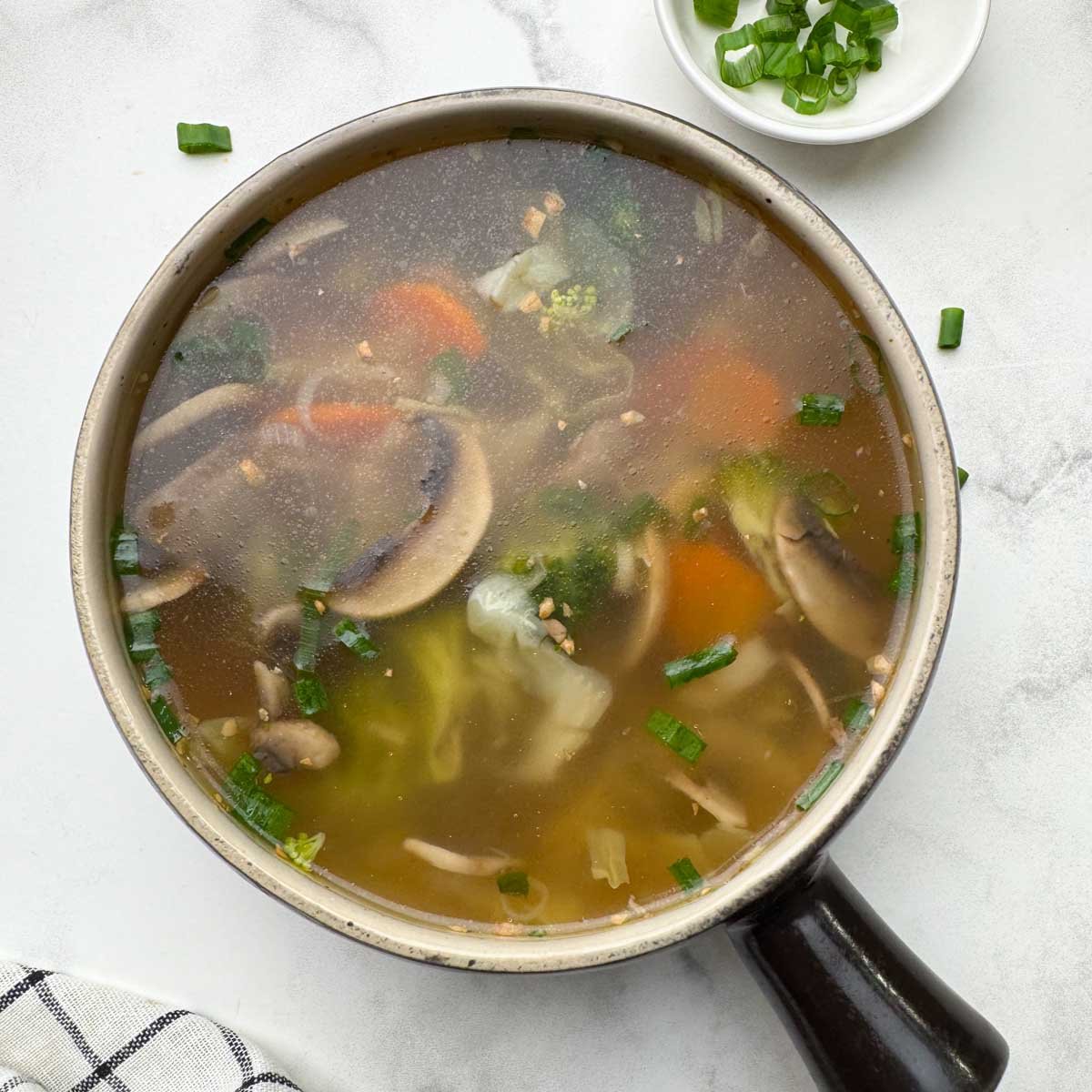 healthy vegetable clear soup served in a soup bowl with spring onions on the side