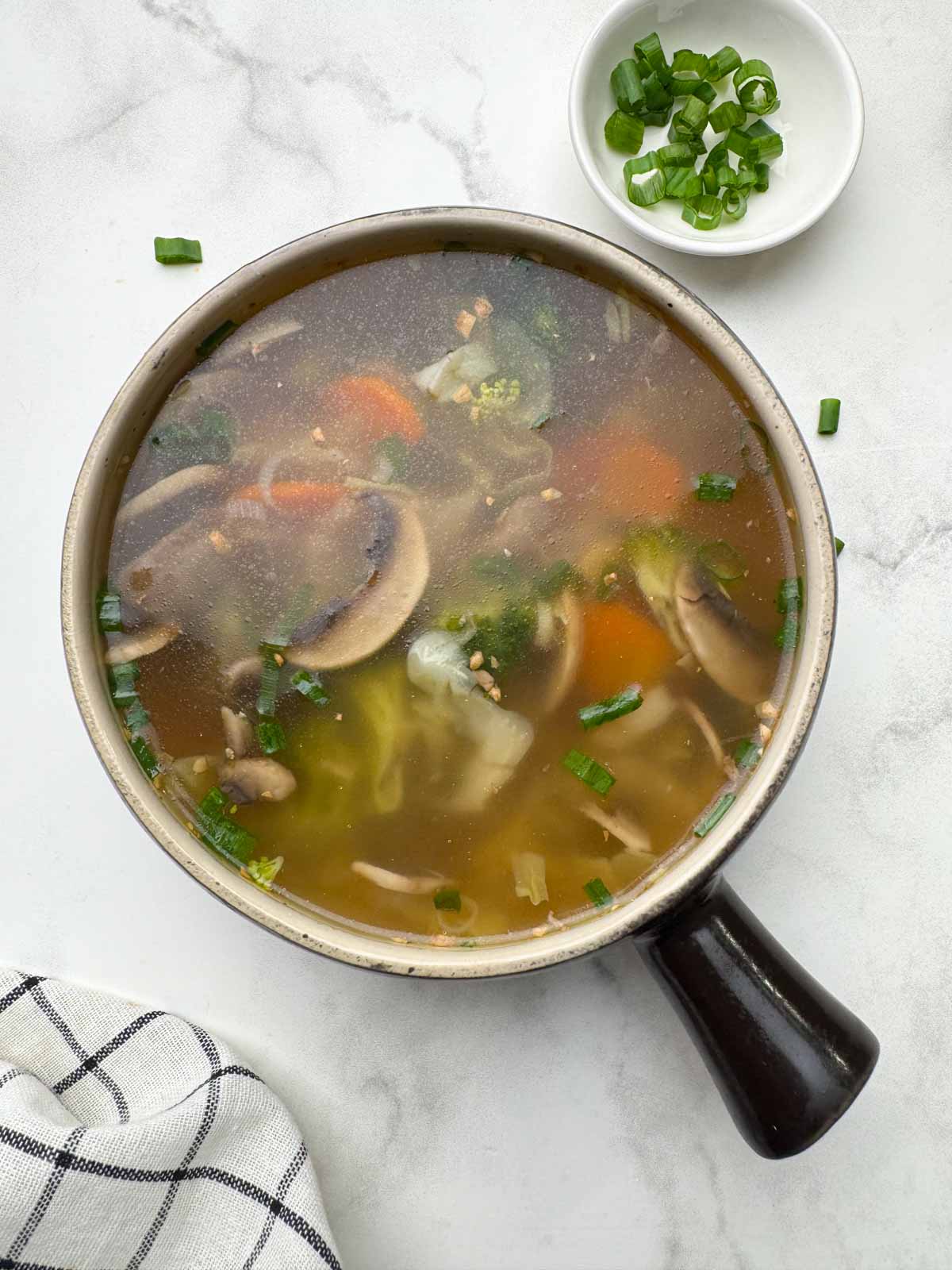 vegetable clear soup served in a soup bowl with spring onions on the side