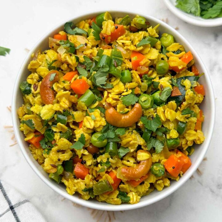 vegetable oats upma served in a bowl with coriander leaves on the side
