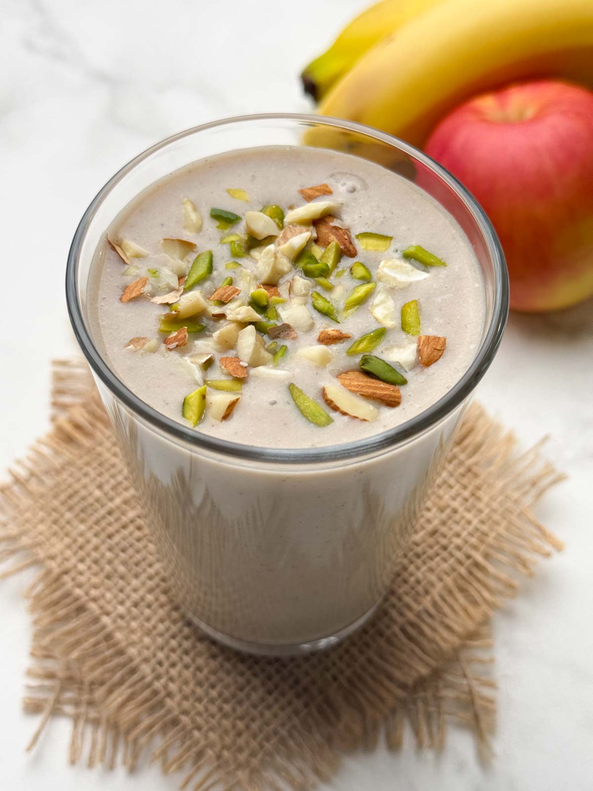 apple banana smoothie in a glass garnished with nuts with fruit in the background