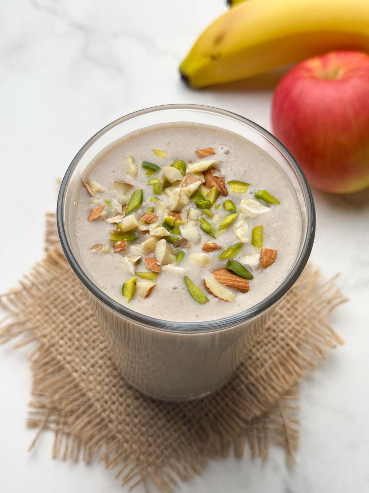 apple banana smoothie in a glass garnished with nuts with fruit in the background