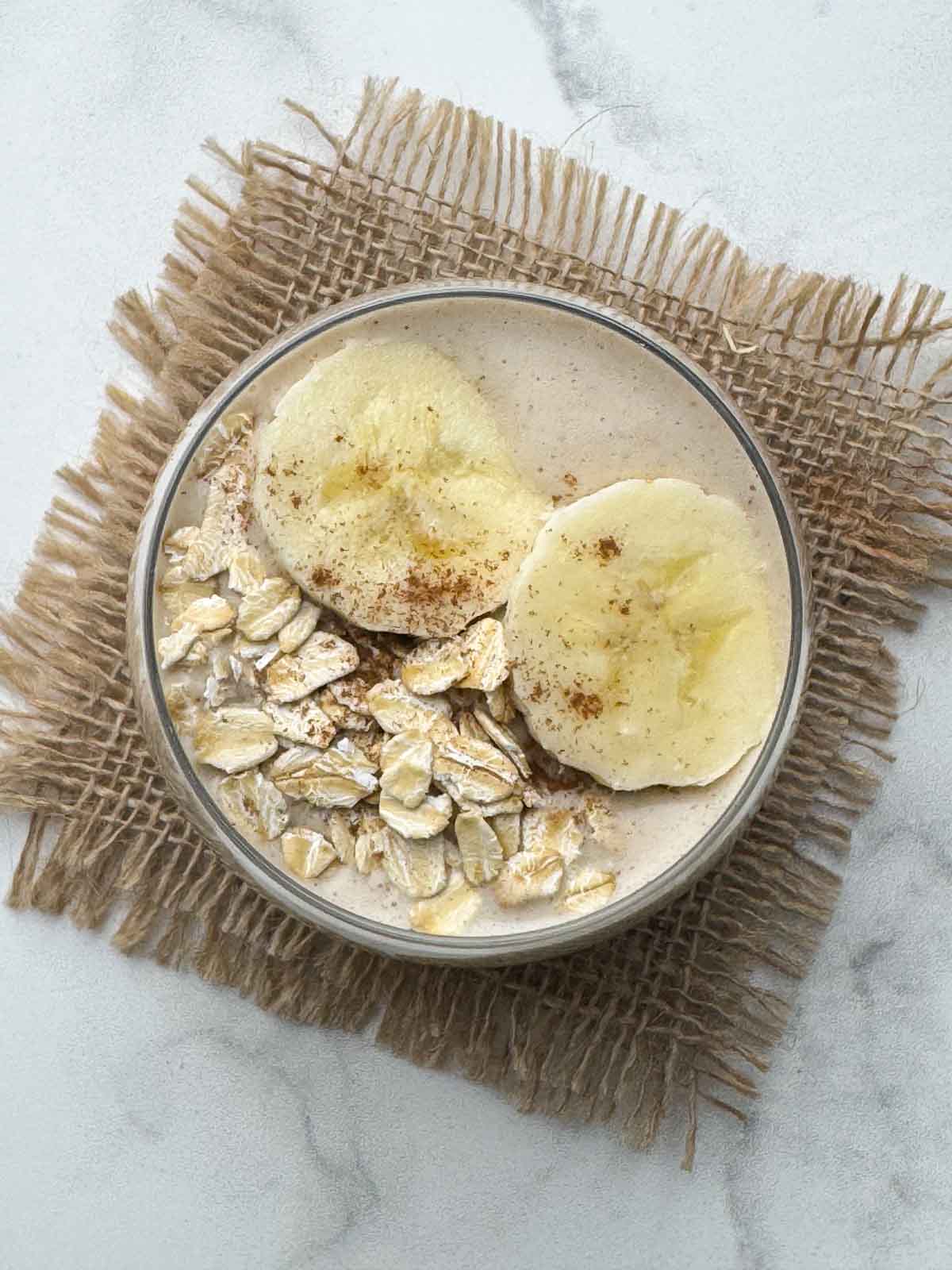 oats smoothie served in a glass topped with oats and banana slices
