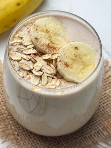 oats banana smoothie served in a glass topped with oats and banana slices