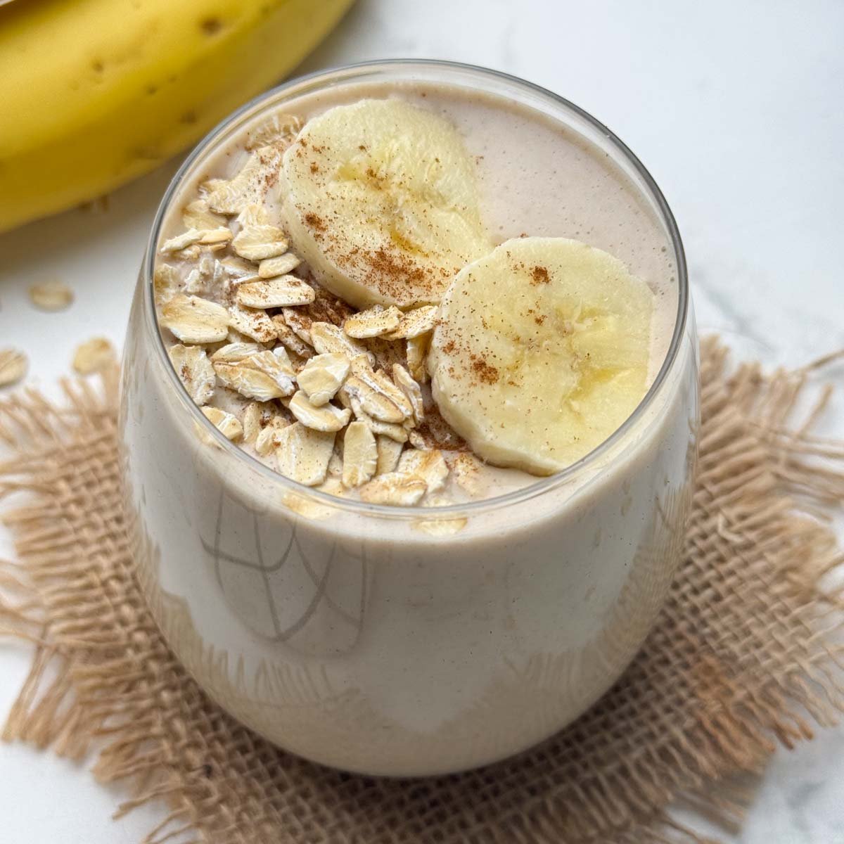 oats banana smoothie served in a glass topped with oats and banana slices