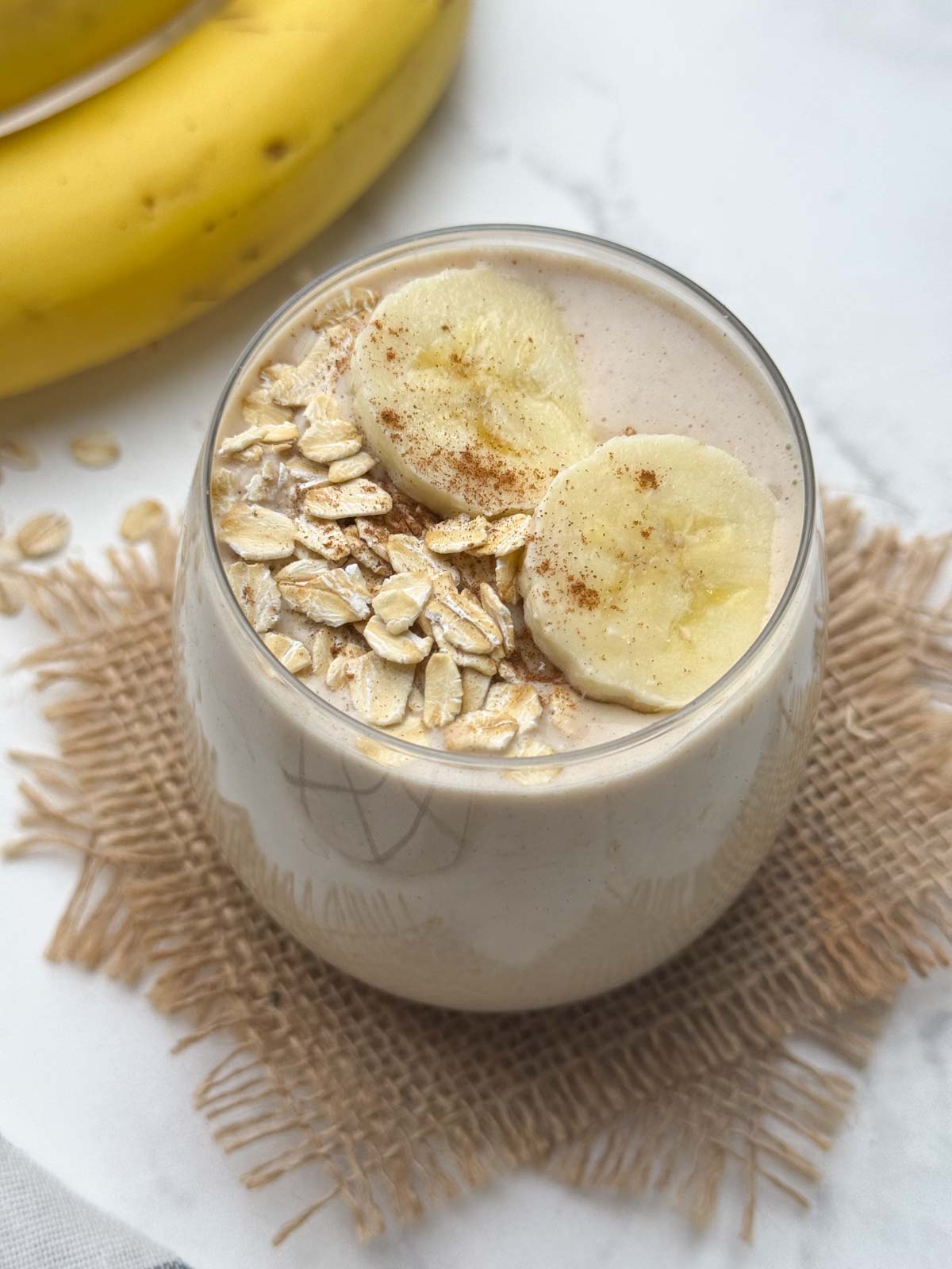 oats banana smoothie served in a glass topped with oats and banana slices