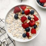 Overnight oats with chia seeds in a white serving bowl with berries and slivered almonds on the top and with one bowl of berries in the side.