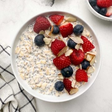 Overnight oats with chia seeds in a white serving bowl with berries and slivered almonds on the top and with one bowl of berries in the side.
