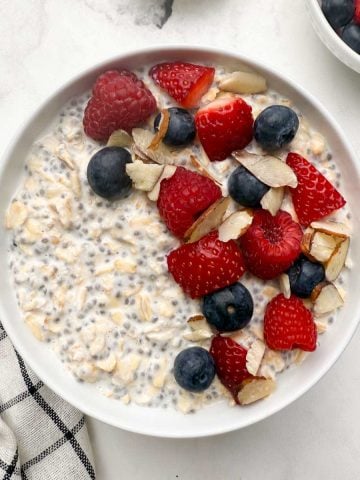 Overnight oats with chia seeds in a white serving bowl with berries and slivered almonds on the top and with one bowl of berries in the side.