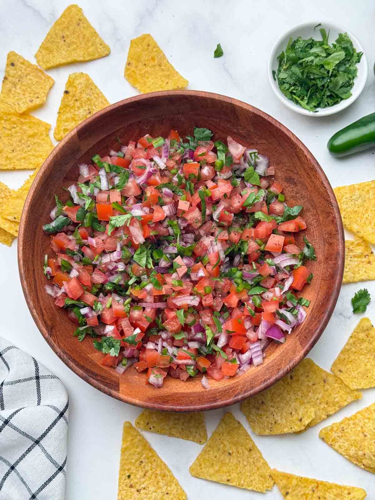 pico de gallo served in a wooden bowl with side of tortilla chips and coriander. 
