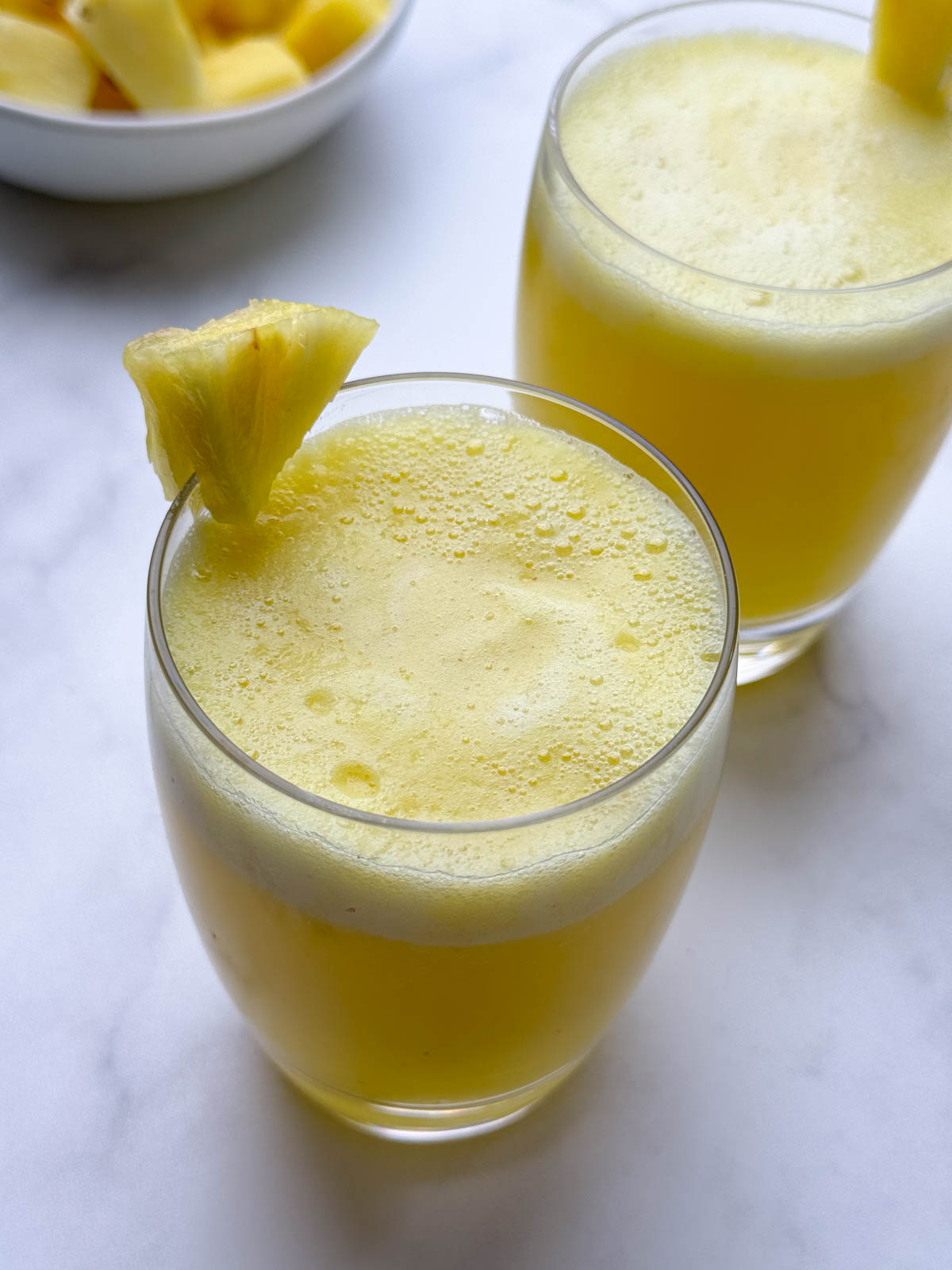 pineapple juice served in two glasses garnished with a piece of pineapple on top