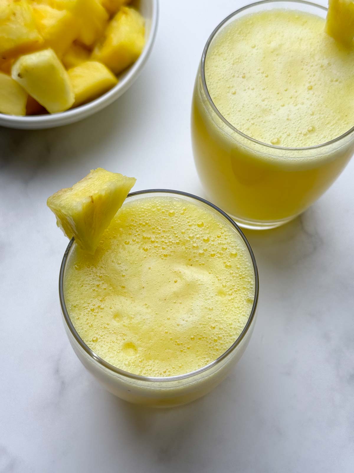 pineapple juice served in two glasses garnished with a piece of pineapple on top