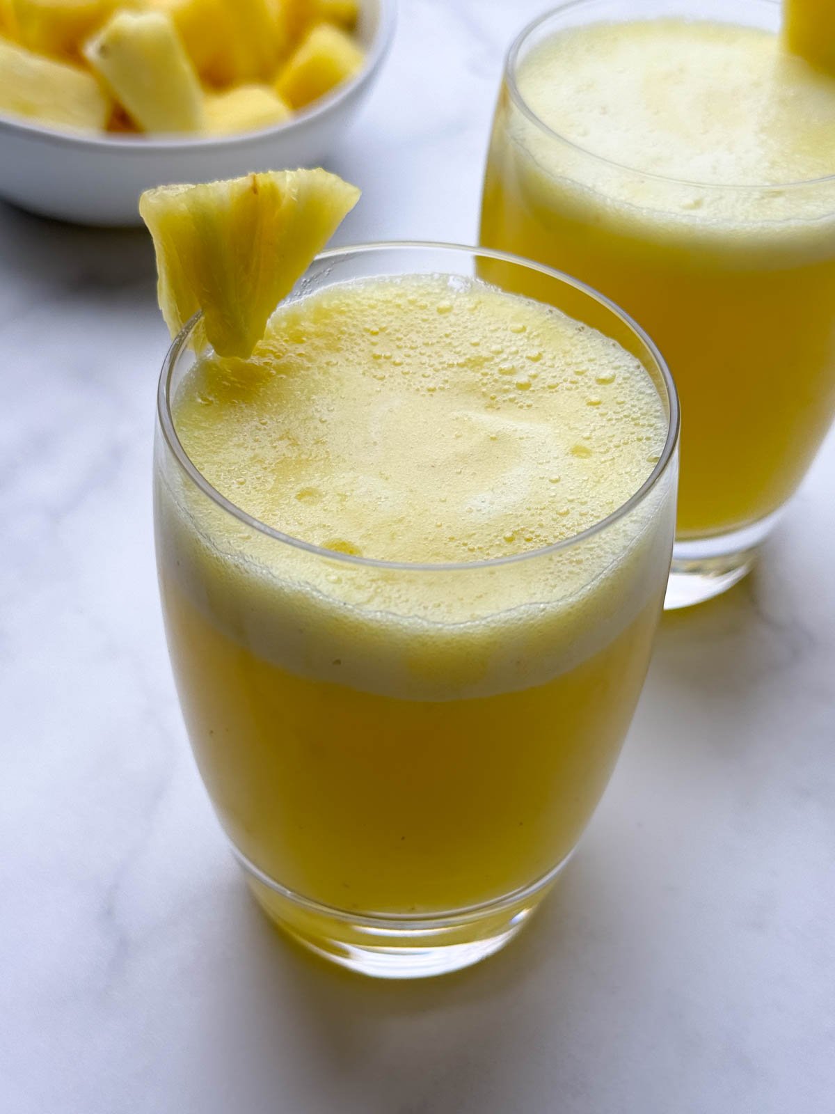 pineapple juice served in two glasses garnished with a piece of pineapple on top