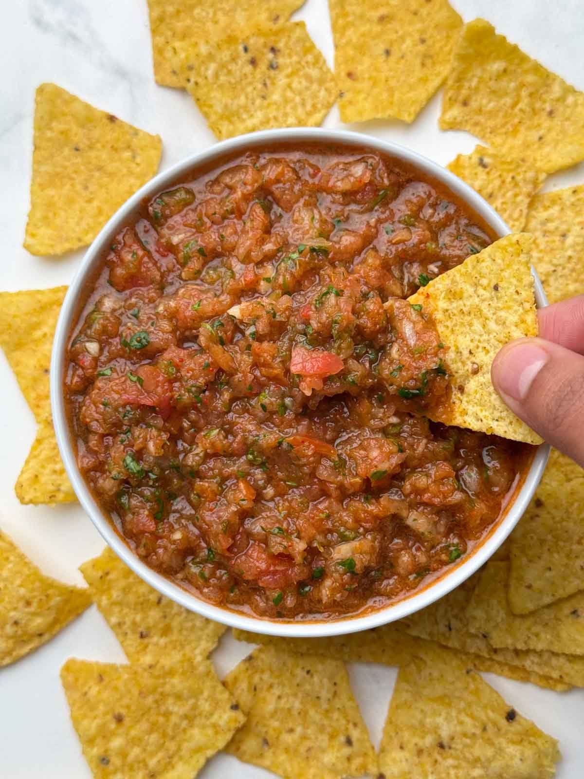 fresh homemade salsa served in a bowl and tortilla chips dipped inside the salsa