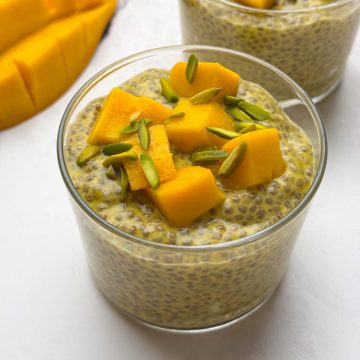 Two glass bowls of mango coconut milk chia pudding topped with diced mango and pistachios along with mango on the side.