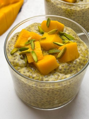 Two glass bowls of mango coconut milk chia pudding topped with diced mango and pistachios along with mango on the side.