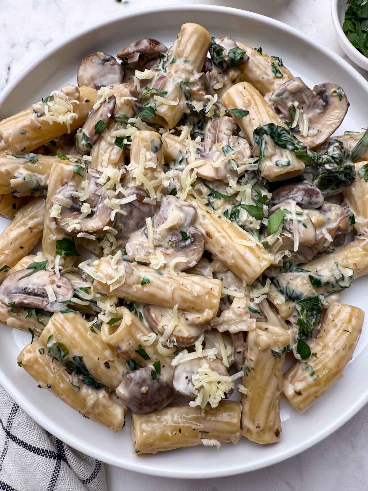 Creamy mushroom spinach pasta served in a plate garnished with cheese.