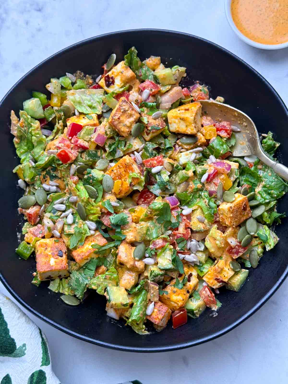 Spicy paneer salad served on a black bowl with fork on it and greek yogurt dressing on the side.