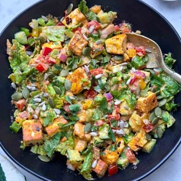 Spicy paneer salad served on a black bowl with fork on it and greek yogurt dressing on the side.