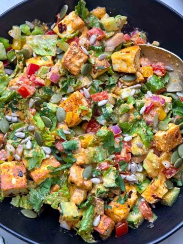 Spicy paneer salad served on a black bowl with fork on it and greek yogurt dressing on the side.