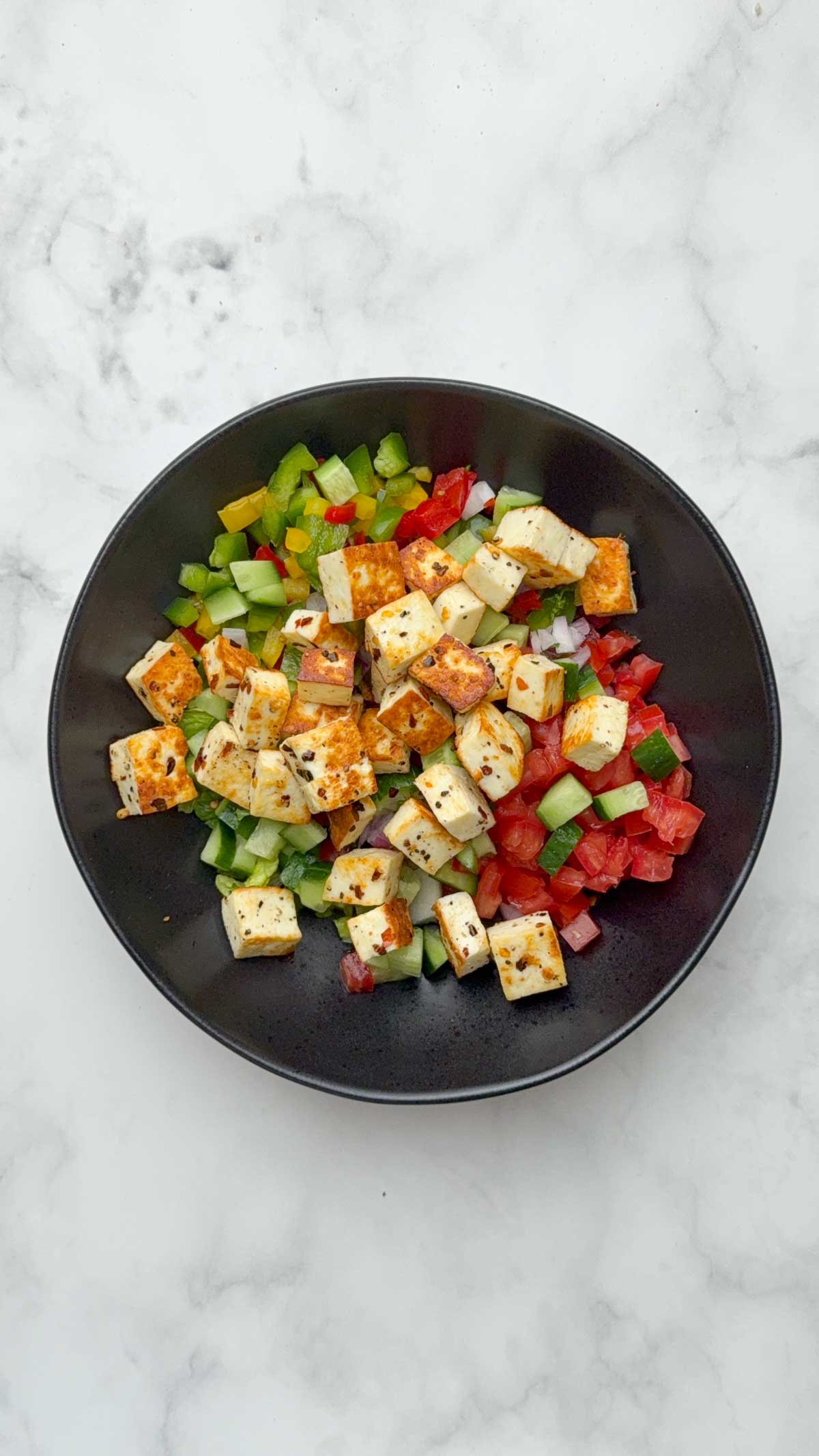 Step to add diced veggies and paneer in a black mixing bowl.