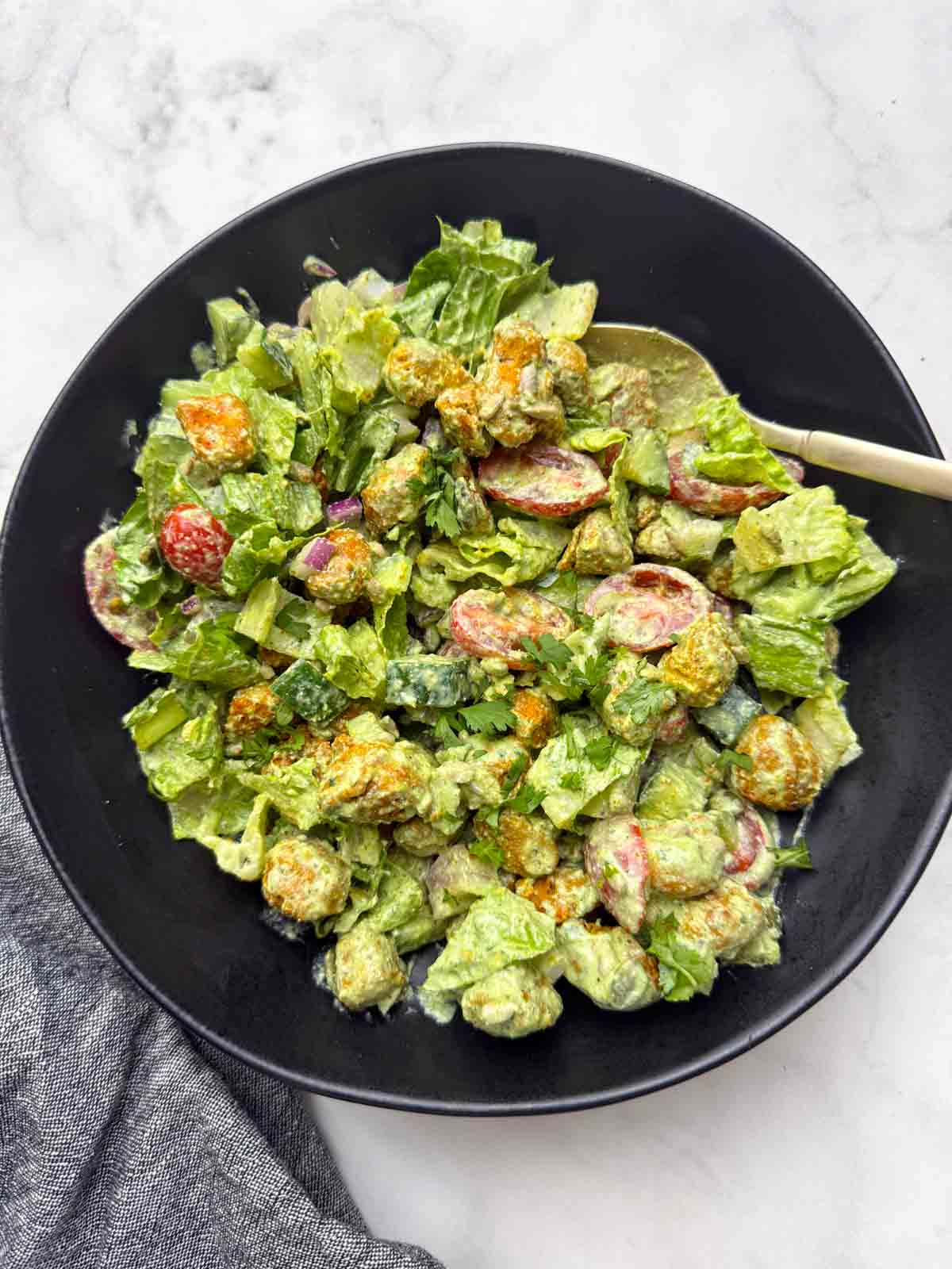 High protein soya chunks salad with greek yogurt dressing on a black bowl with a golden spoon on it.