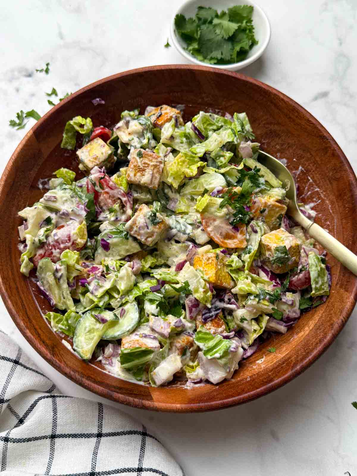 tofu salad mixed in a wooden bowl with a golden spoon on top and coriander leaves in a bowl on the side.