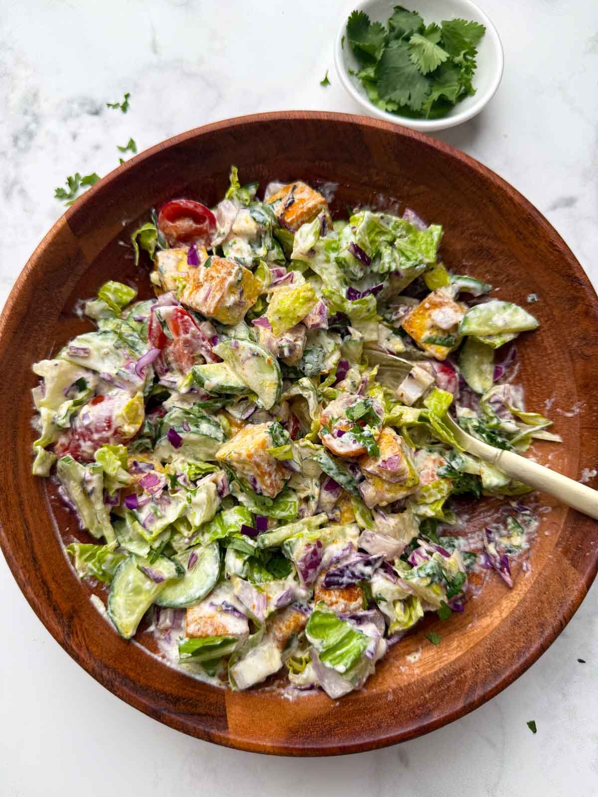 Tofu salad with yogurt dressing in a wooden bowl and spoon on it.