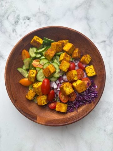Lettuce, veggies and pan fried tofu in a wooden bowl.