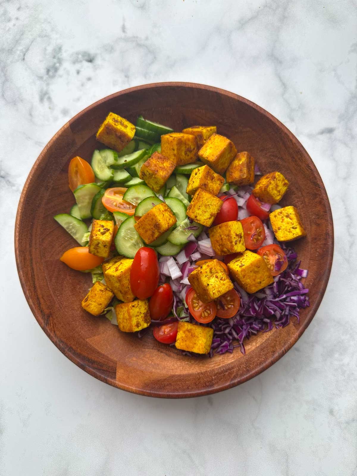 Lettuce, veggies and pan fried tofu in a wooden bowl.