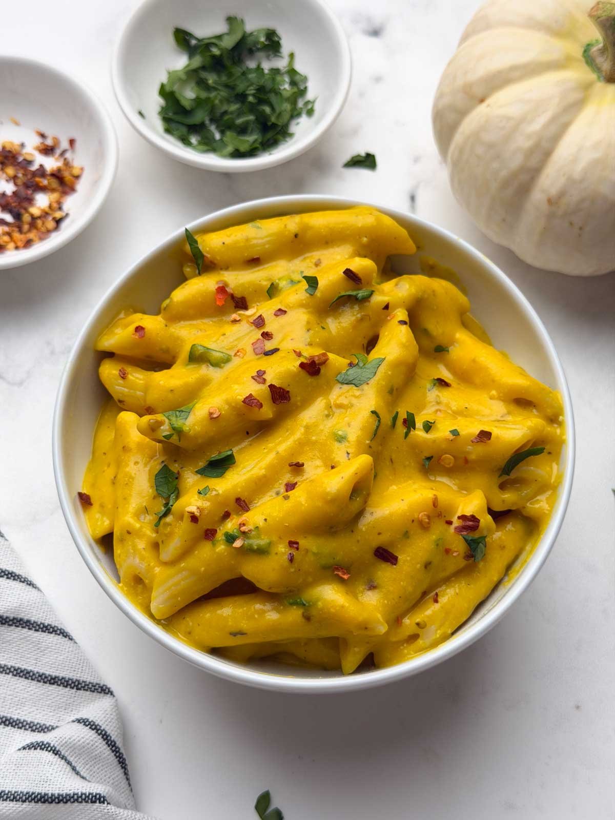Pumpkin pasta served in a bowl with chili flakes, parsley, and decorative pumpkin on the side.