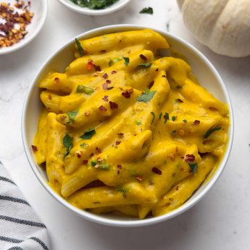 Pumpkin pasta served in a bowl with chili flakes, parsley, and decorative pumpkin on the side.