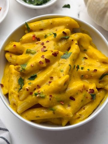Pumpkin pasta served in a bowl with chili flakes, parsley, and decorative pumpkin on the side.