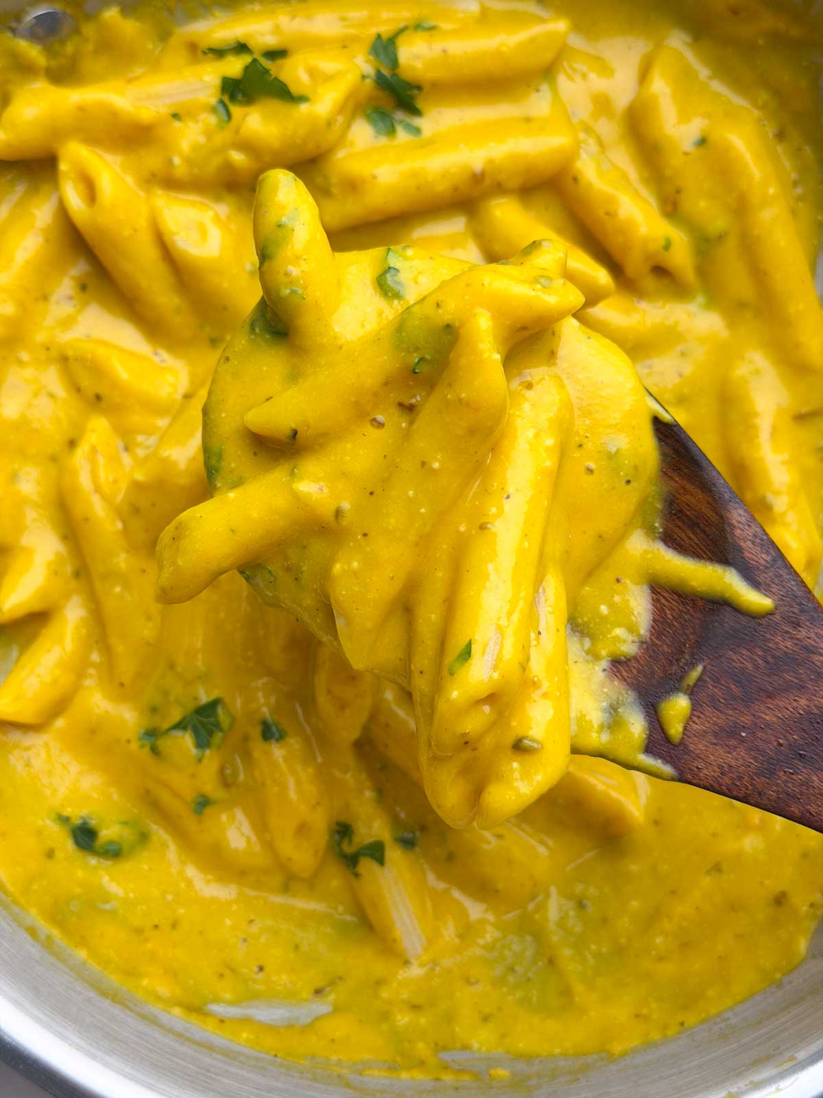Creamy pumpkin pasta served in a steel kadai, with a spoon lifting a portion of the pasta.