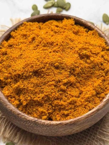 Pumpkin Seeds Chutney Powder served in a wooden bowl with pumpkin seeds on the surface for decoration.