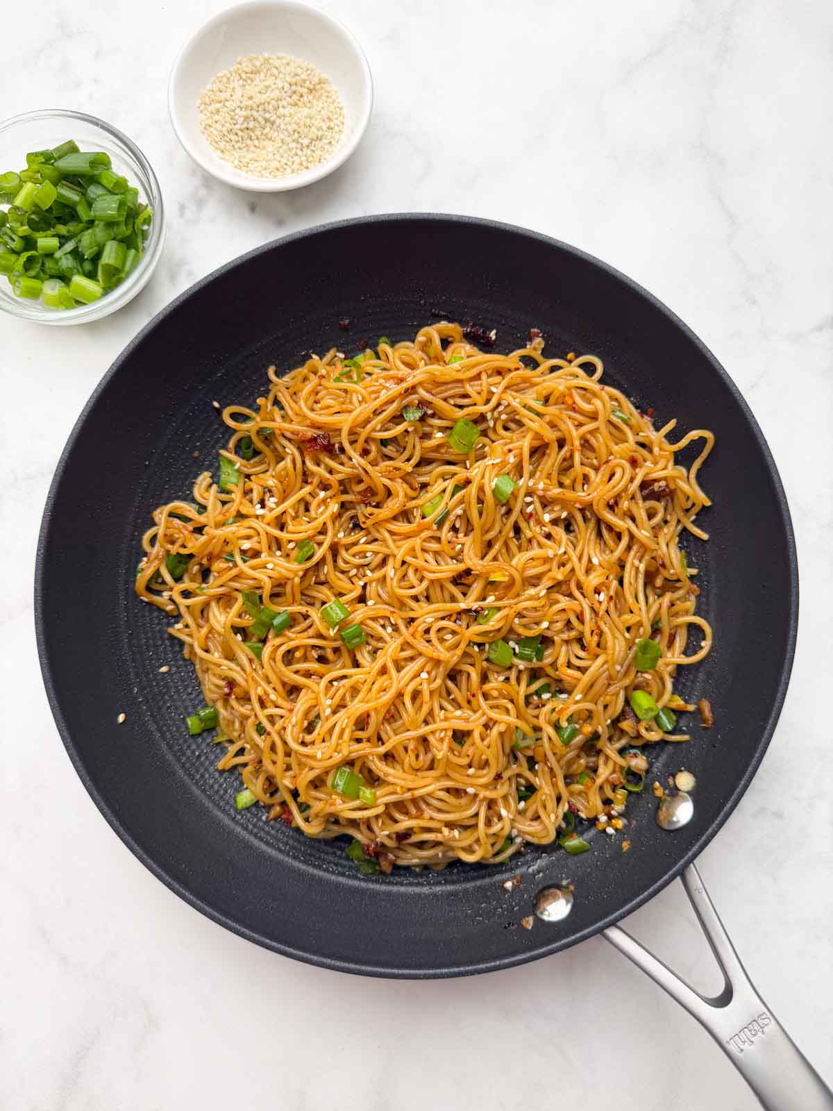 Spicy Chili garlic oil noodles on a skillet with sesame seeds and spring onions on the side in a bowl.