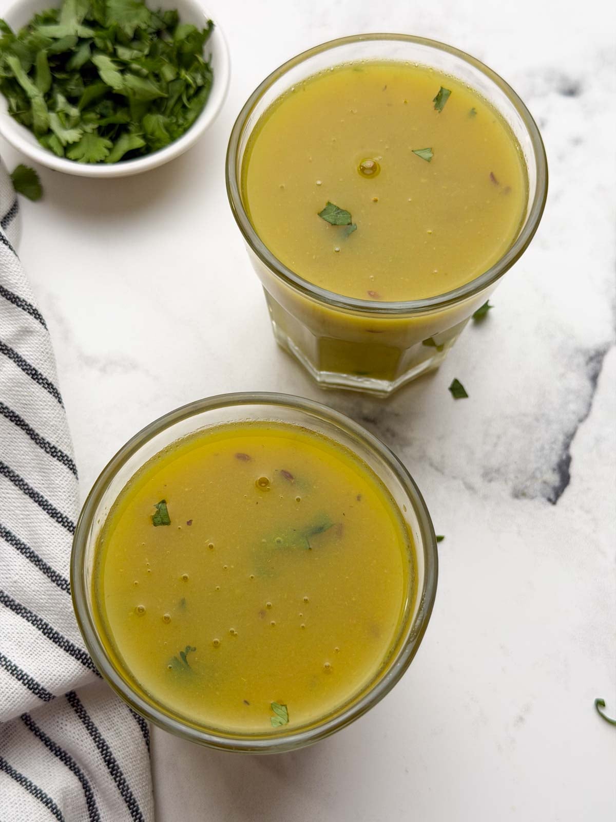 Drumstick moong soup served in two glass containers with coriander leaves on the side for garnish.