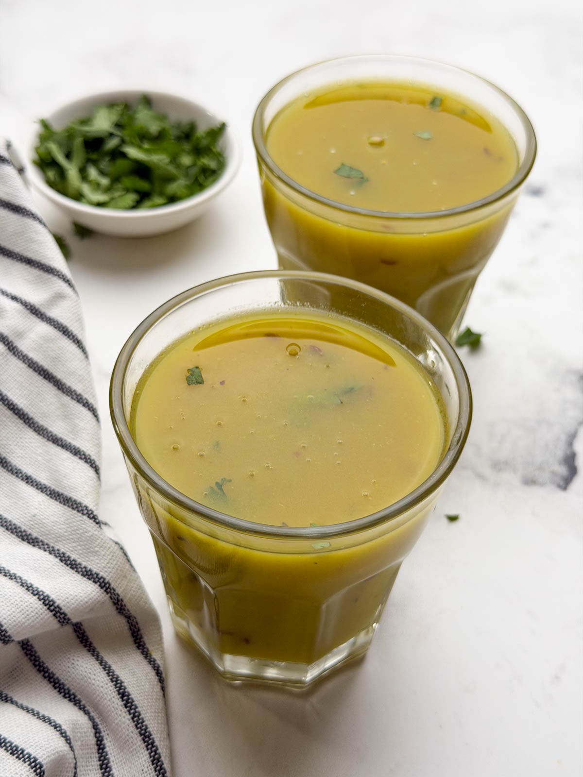 Drumstick pods soup served in two glass containers with coriander leaves as garnish.
