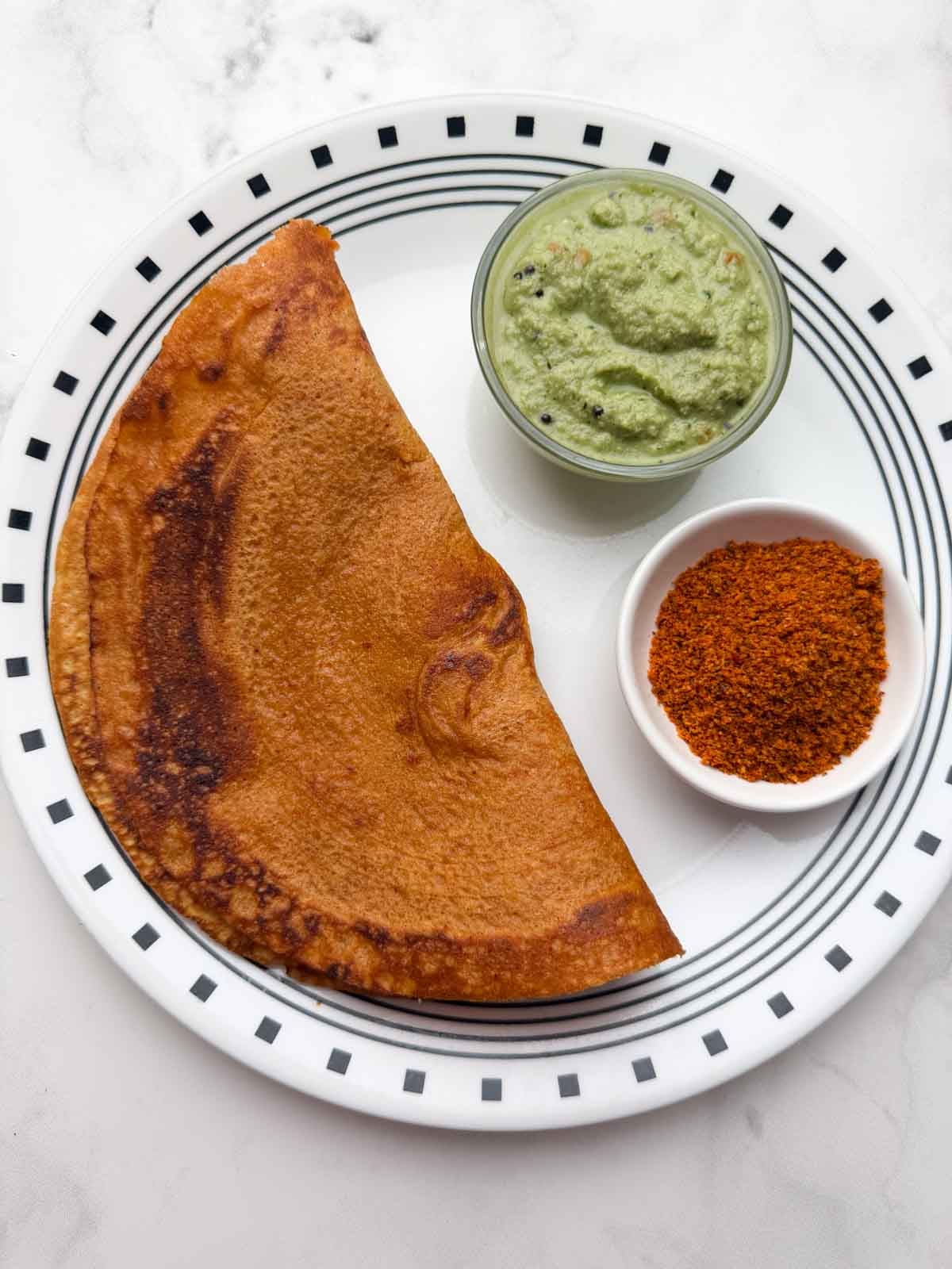 Masoor quinoa dosa on a plate with coconut chutney and chutney powder on the side.