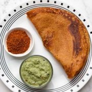Masoor dal quinoa dosa on a plate with coconut chutney and chutney powder on the side.