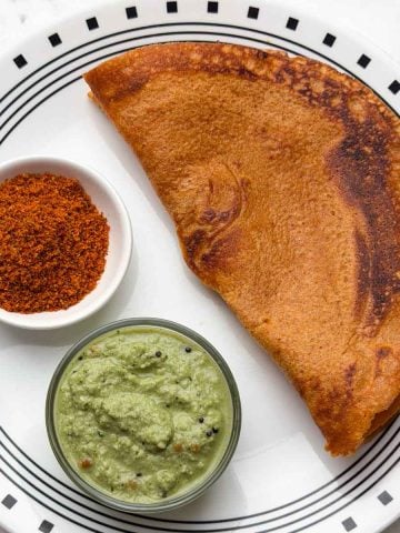 Masoor dal quinoa dosa on a plate with coconut chutney and chutney powder on the side.