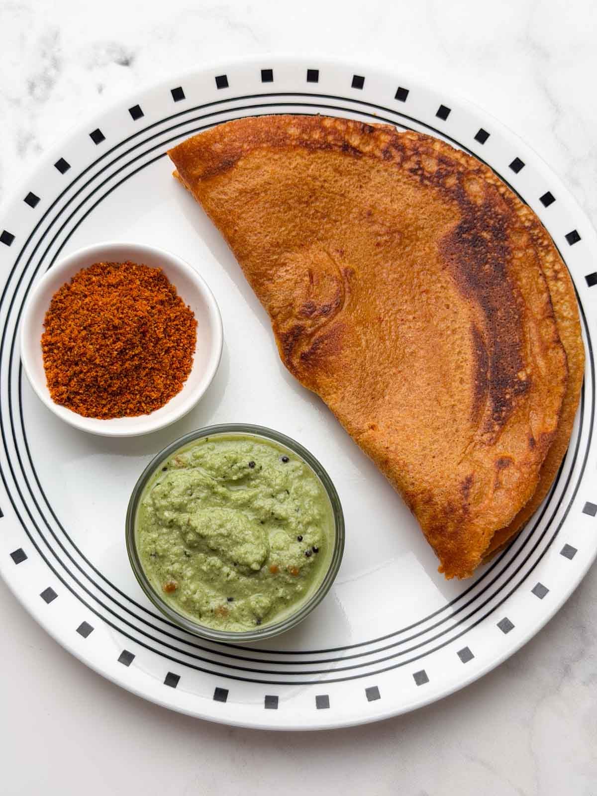 Masoor quinoa dosa on a plate with coconut chutney and chutney powder on the side.