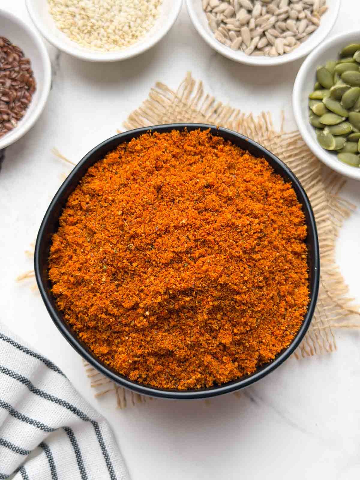 A black bowl full of mixed seeds chutney powder and sesame, flax, sunflower and pumpkin seeds on the side in small individual bowls for decoration.