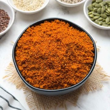 A black bowl full of mixed seeds chutney powder and sesame, flax, sunflower and pumpkin seeds on the side in small individual bowls for decoration.