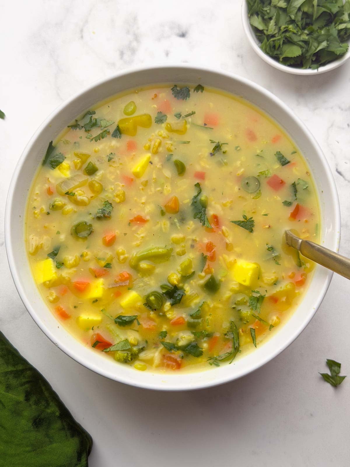 A bowl of oats soup with a spoon in it and coriander leaves on the side for garnish.
