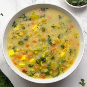 Vegetable Oats soup in a white bowl with coriander leaves on the side.