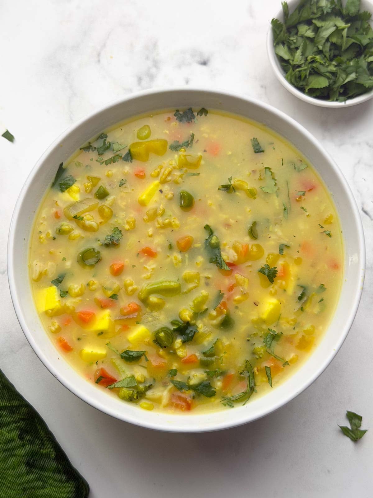 Oats soup in a white bowl with coriander leaves on the side.