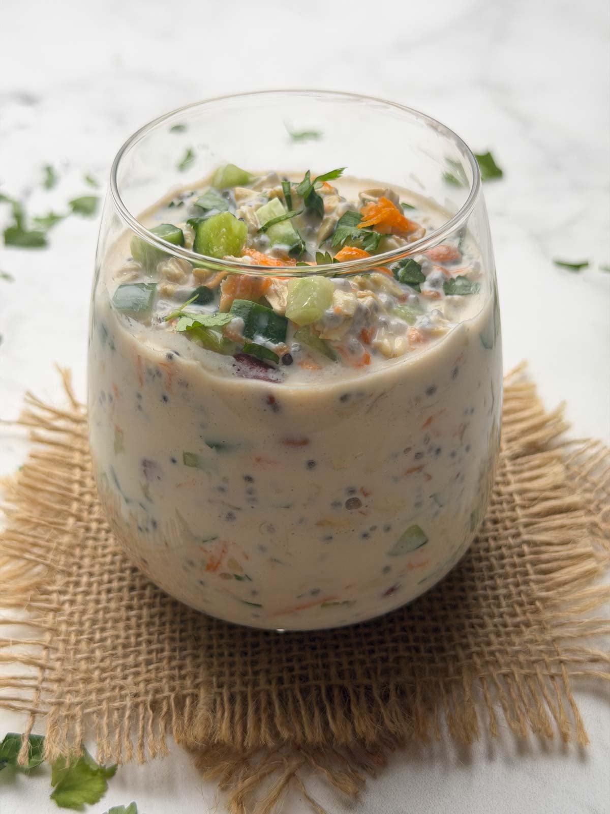 Overnight oats chia tadka in a glass bowl garnished with chopped cucumber, carrot.
